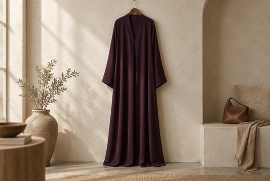 Robe longue en crêpe aubergine suspendue devant un mur crème
